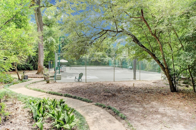 surrounding community with a tennis court, fence, and view of scattered trees