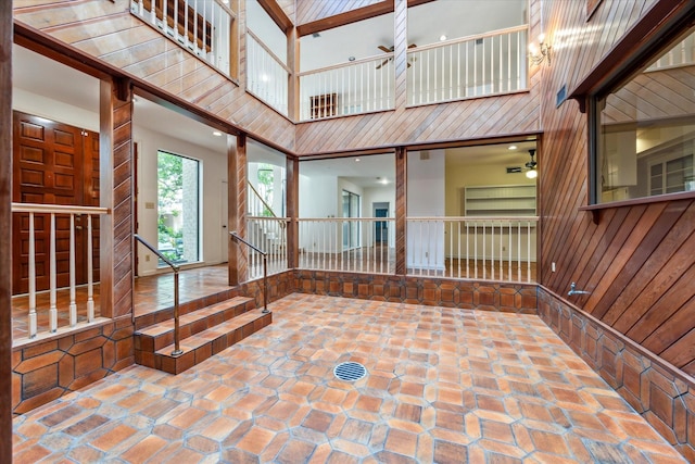 foyer featuring a high ceiling, ceiling fan, and wood walls