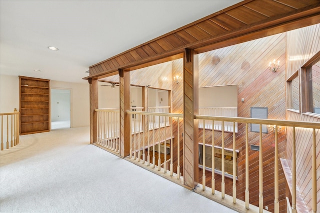 corridor with carpet floors, an upstairs landing, wood walls, and recessed lighting