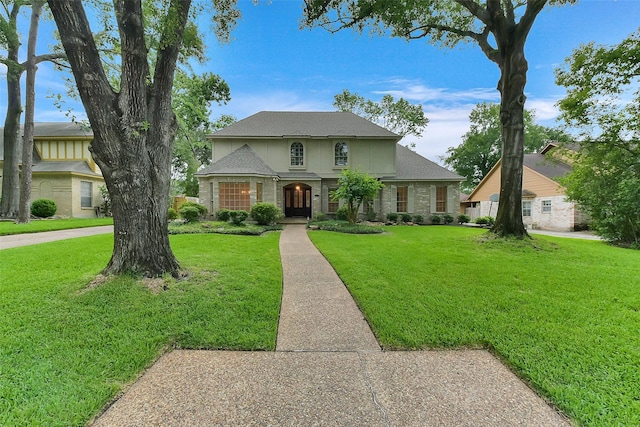 traditional-style home featuring a front lawn, roof with shingles, and brick siding