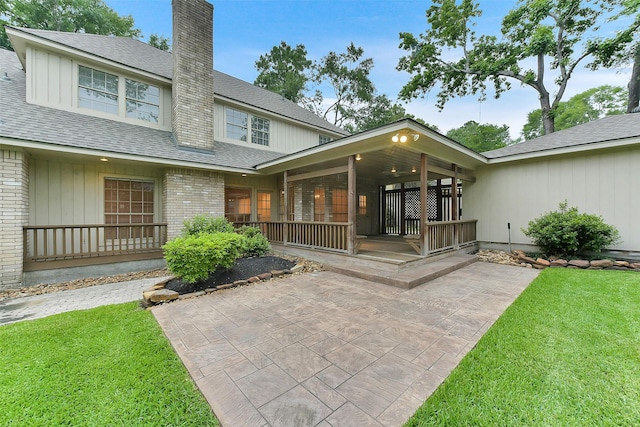 back of property featuring a yard, a chimney, roof with shingles, and a patio area