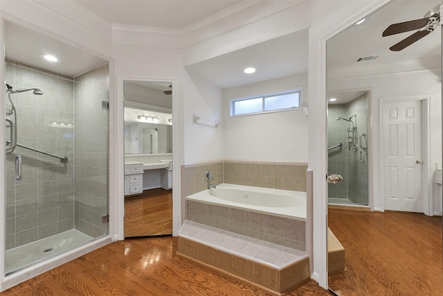 full bathroom featuring ceiling fan, a stall shower, a garden tub, crown molding, and wood finished floors