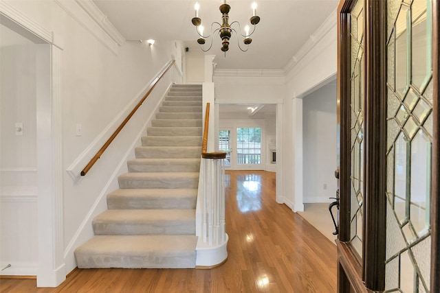 foyer entrance with crown molding, stairway, wood finished floors, a chandelier, and baseboards