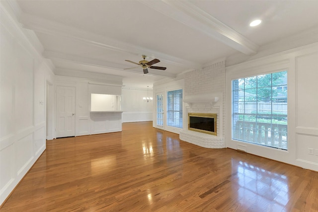 unfurnished living room with a decorative wall, beam ceiling, crown molding, a fireplace, and wood finished floors