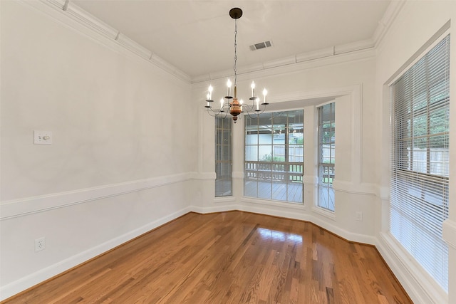 unfurnished dining area with a chandelier, plenty of natural light, crown molding, wood finished floors, and baseboards