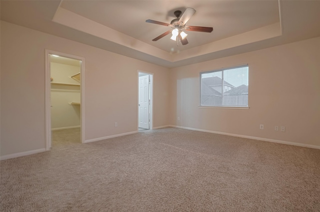 carpeted empty room featuring a tray ceiling, a ceiling fan, and baseboards