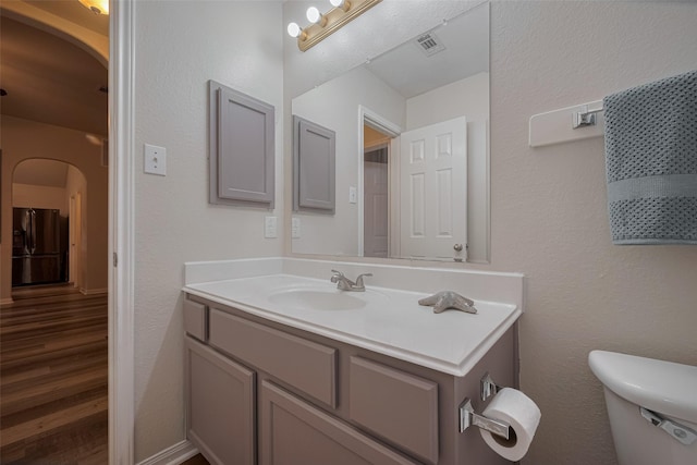 half bath featuring wood finished floors, toilet, and vanity