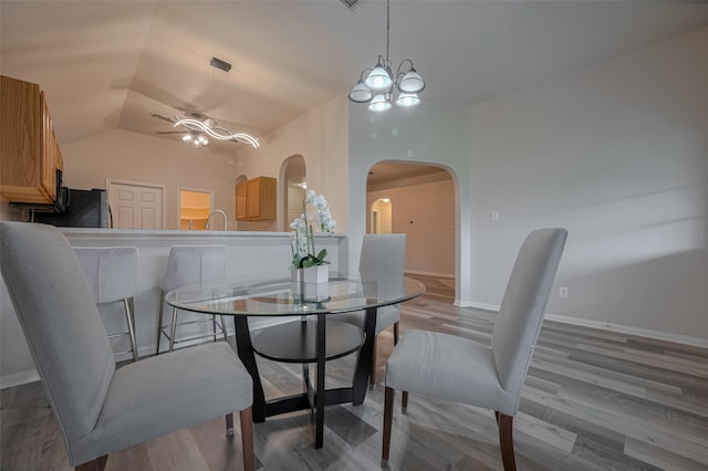 dining room featuring arched walkways, a ceiling fan, wood finished floors, baseboards, and lofted ceiling