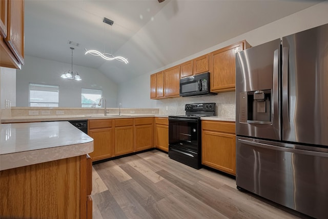 kitchen featuring black appliances, a sink, a chandelier, light wood-style flooring, and a peninsula