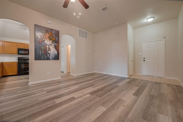 unfurnished living room with arched walkways, a ceiling fan, light wood finished floors, and baseboards
