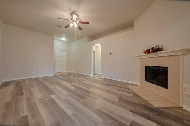 unfurnished living room with arched walkways, a ceiling fan, a fireplace, light wood-style flooring, and baseboards