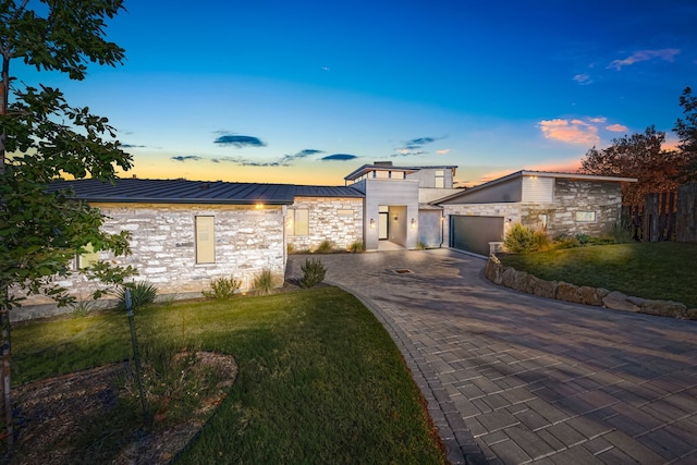 contemporary house with stone siding, a garage, a standing seam roof, decorative driveway, and a lawn