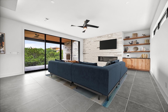 living room with ceiling fan, tile patterned flooring, a stone fireplace, and baseboards