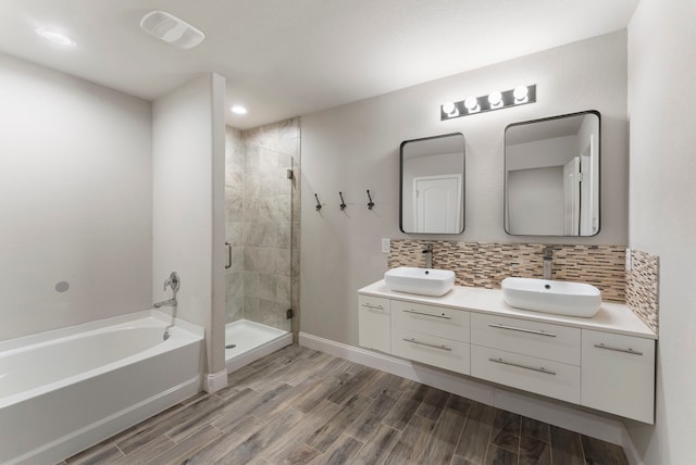 bathroom featuring a stall shower, wood finished floors, tasteful backsplash, a garden tub, and double vanity
