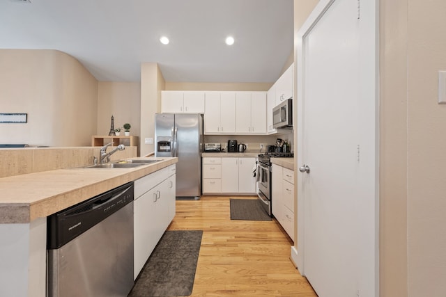kitchen with appliances with stainless steel finishes, white cabinets, light wood-style floors, light countertops, and a center island with sink