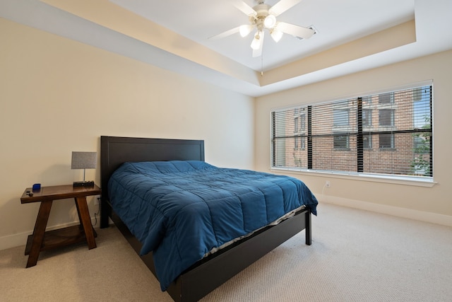 carpeted bedroom featuring baseboards, a raised ceiling, and ceiling fan