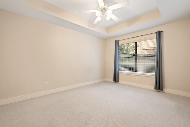 spare room featuring a tray ceiling, baseboards, light carpet, and a ceiling fan
