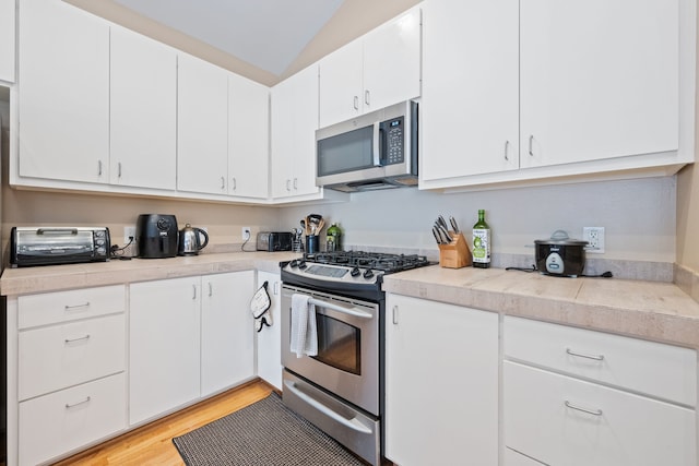 kitchen with stainless steel appliances, light countertops, white cabinetry, light wood-style flooring, and lofted ceiling