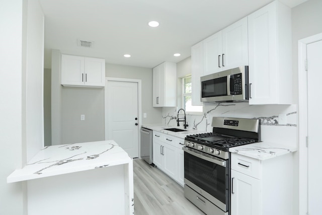 5506 Karelian Dr, Houston, TX 77091 - kitchen featuring stainless steel appliances, a sink, light stone countertops, light wood-style floors, and white cabinets