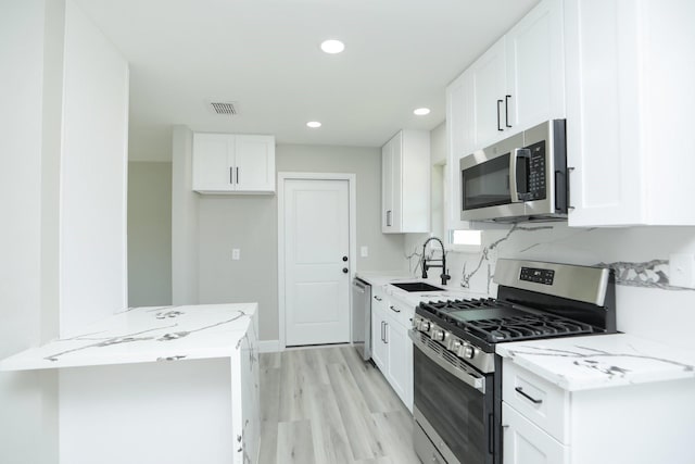 5506 Karelian Dr, Houston, TX 77091 - kitchen featuring stainless steel appliances, a sink, light stone counters, light wood finished floors, and white cabinetry