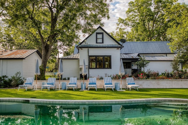 rear view of house featuring an outdoor pool, a lawn, metal roof, and a standing seam roof