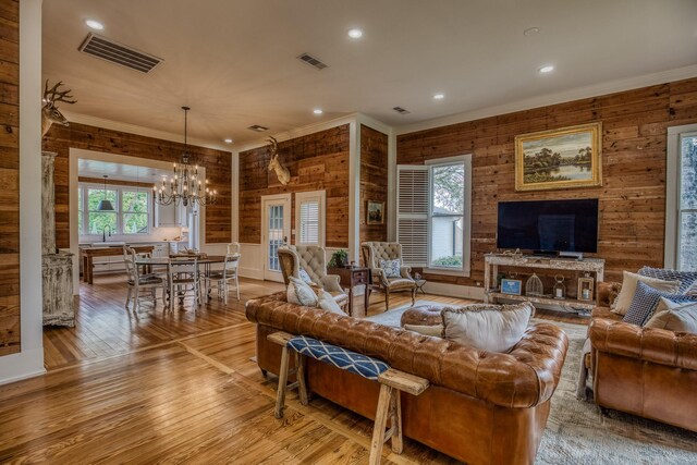 living area with light wood finished floors, crown molding, a chandelier, recessed lighting, and wood walls