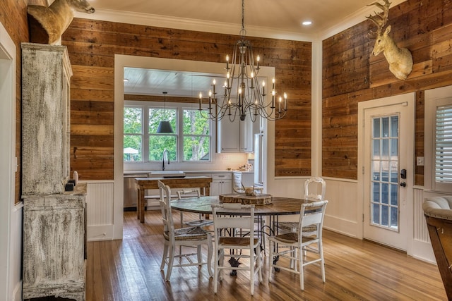 dining area featuring light wood finished floors, wood walls, ornamental molding, and a chandelier