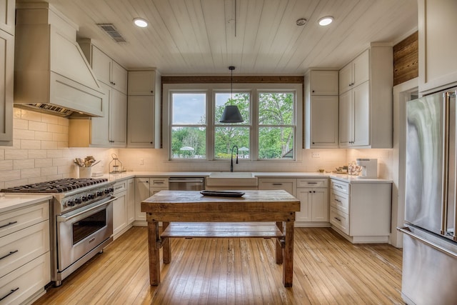 kitchen with appliances with stainless steel finishes, a sink, premium range hood, light countertops, and recessed lighting