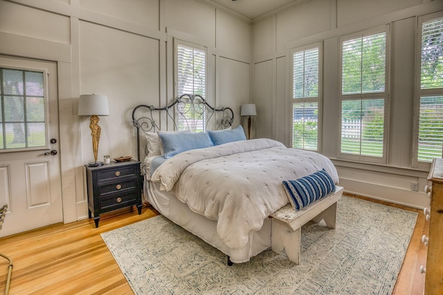 bedroom featuring a decorative wall, multiple windows, light wood-style flooring, and ornamental molding