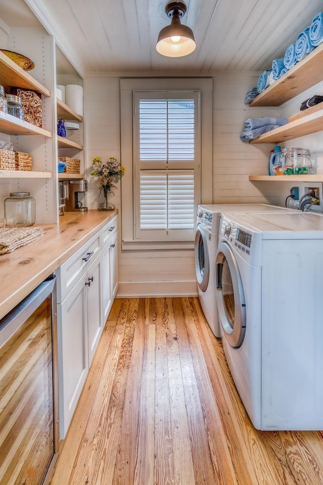 clothes washing area featuring beverage cooler, cabinet space, light wood-style floors, washer and clothes dryer, and wood ceiling