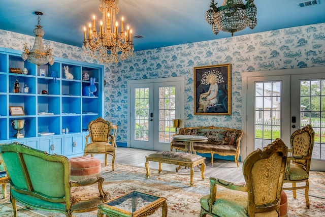 sitting room with french doors, a chandelier, wallpapered walls, wood finished floors, and healthy amount of natural light