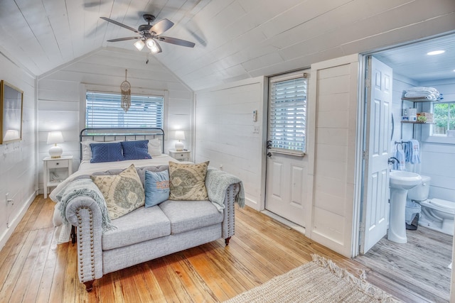 bedroom with light wood-style floors, lofted ceiling, ensuite bathroom, wood walls, and ceiling fan
