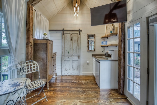 kitchen featuring dark wood-style floors, a barn door, wooden walls, stainless steel dishwasher, and lofted ceiling