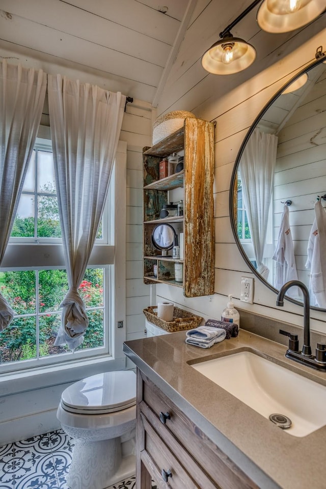 bathroom featuring wood walls, lofted ceiling, vanity, toilet, and tile patterned floors