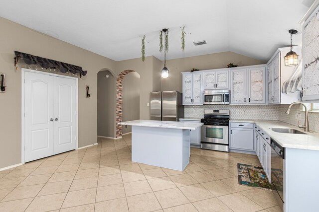 kitchen with stainless steel appliances, a sink, arched walkways, backsplash, and lofted ceiling