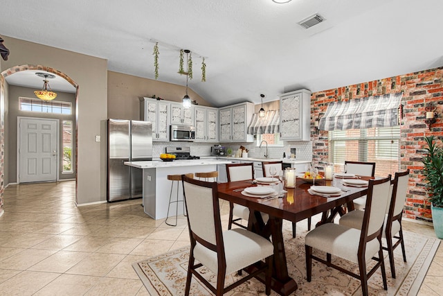 dining space with arched walkways, light tile patterned floors, lofted ceiling, and baseboards