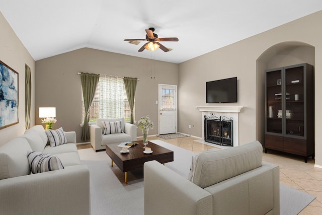 living area featuring light tile patterned floors, ceiling fan, a fireplace, lofted ceiling, and baseboards
