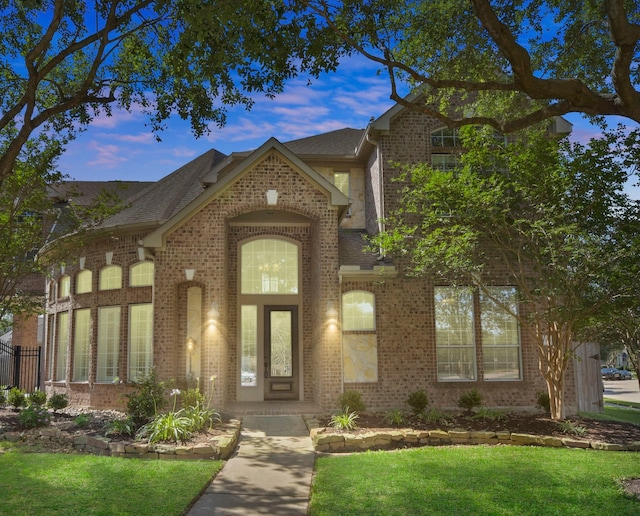8611 Springmere Ct, Houston, TX 77095 - exterior entry at dusk featuring brick siding, a yard, and a shingled roof
