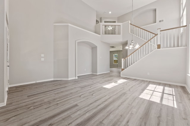 unfurnished living room with a chandelier, stairway, baseboards, wood finished floors, and a high ceiling