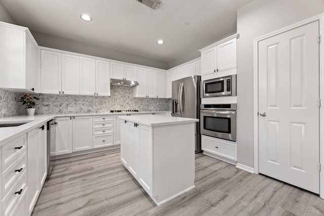 kitchen with stainless steel appliances, under cabinet range hood, light wood-style flooring, white cabinetry, and decorative backsplash