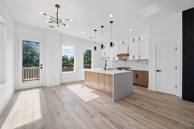 kitchen with a chandelier, light wood finished floors, backsplash, a center island with sink, and recessed lighting