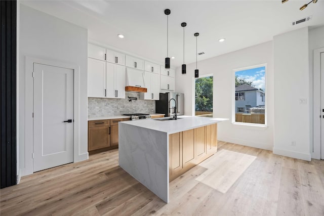 kitchen with light wood-style floors, an island with sink, decorative backsplash, stainless steel fridge, and recessed lighting
