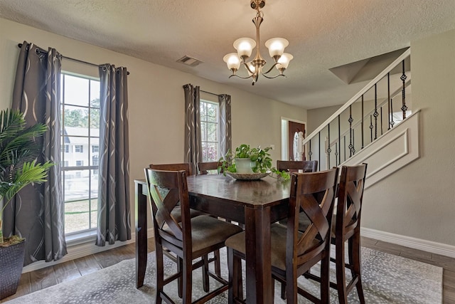 dining area featuring a chandelier, a textured ceiling, wood finished floors, stairs, and baseboards