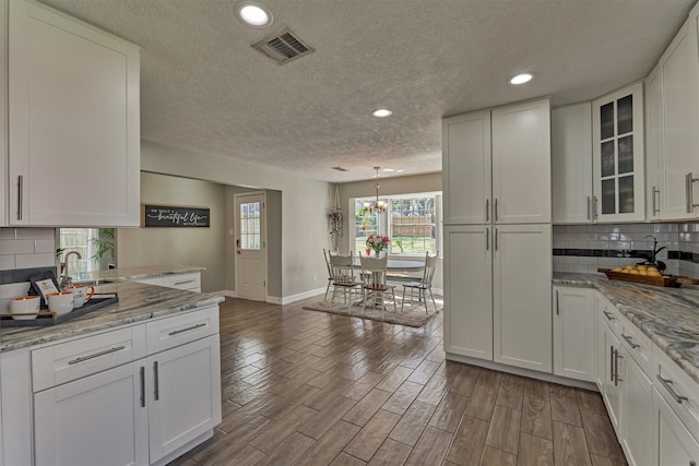 kitchen featuring a textured ceiling, baseboards, a sink, white cabinets, and tasteful backsplash