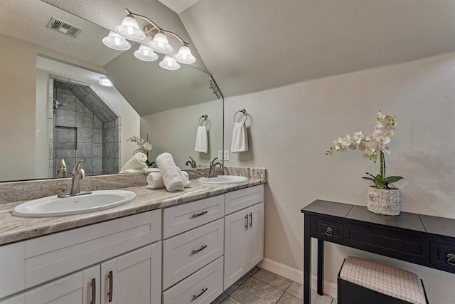 full bath featuring lofted ceiling, double vanity, tiled shower, tile patterned flooring, and baseboards