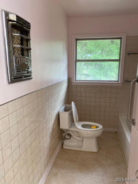 1912 18th St, Huntsville, TX 77340 - bathroom featuring toilet, plenty of natural light, tile walls, wainscoting, and tile patterned floors