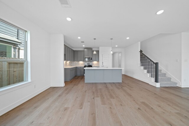 15198 Prairie Mill Dr, New Caney, TX 77357 - kitchen featuring gray cabinets, stainless steel microwave, light countertops, light wood finished floors, and backsplash