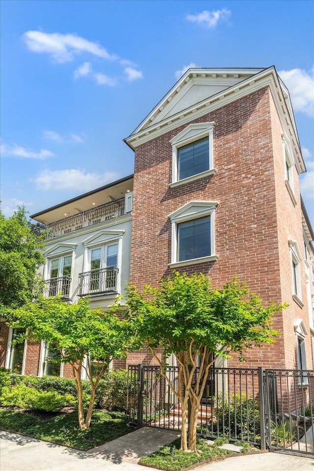 view of front of property with brick siding, fence, and a balcony
