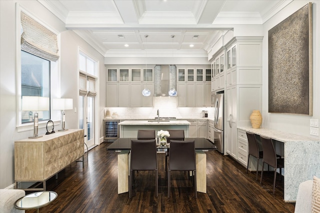 kitchen featuring wall chimney range hood, wine cooler, a kitchen island with sink, dark wood-style floors, and freestanding refrigerator