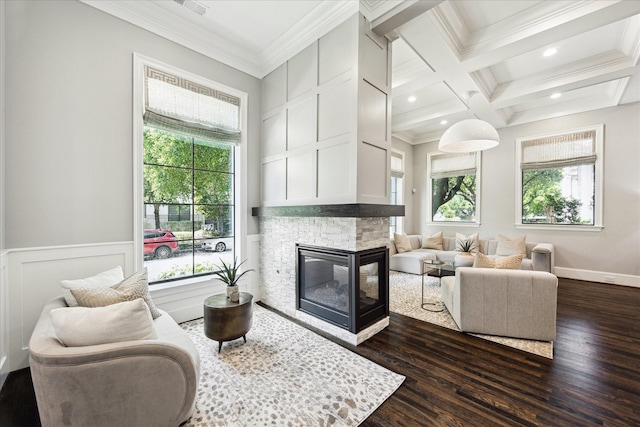 living room featuring healthy amount of natural light, ornamental molding, dark wood finished floors, beam ceiling, and a stone fireplace